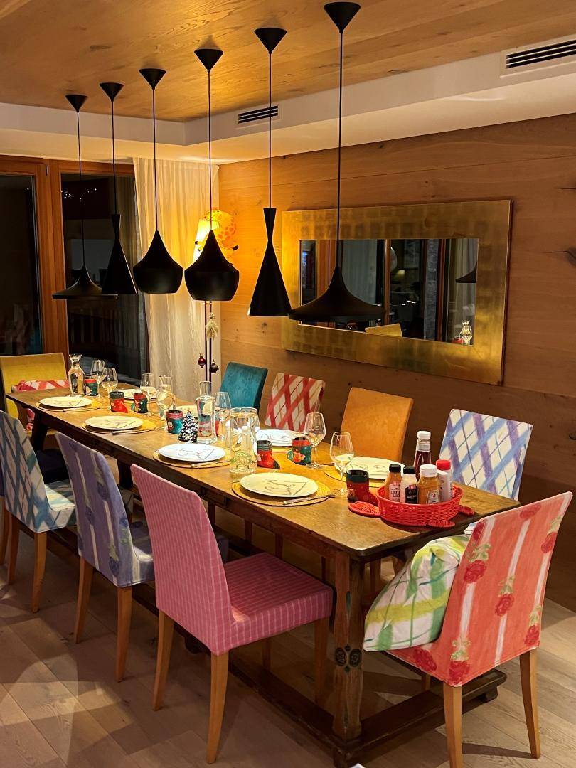 Esszimmer mit großem Holztisch, bunten Stühlen und modernen Pendelleuchten.