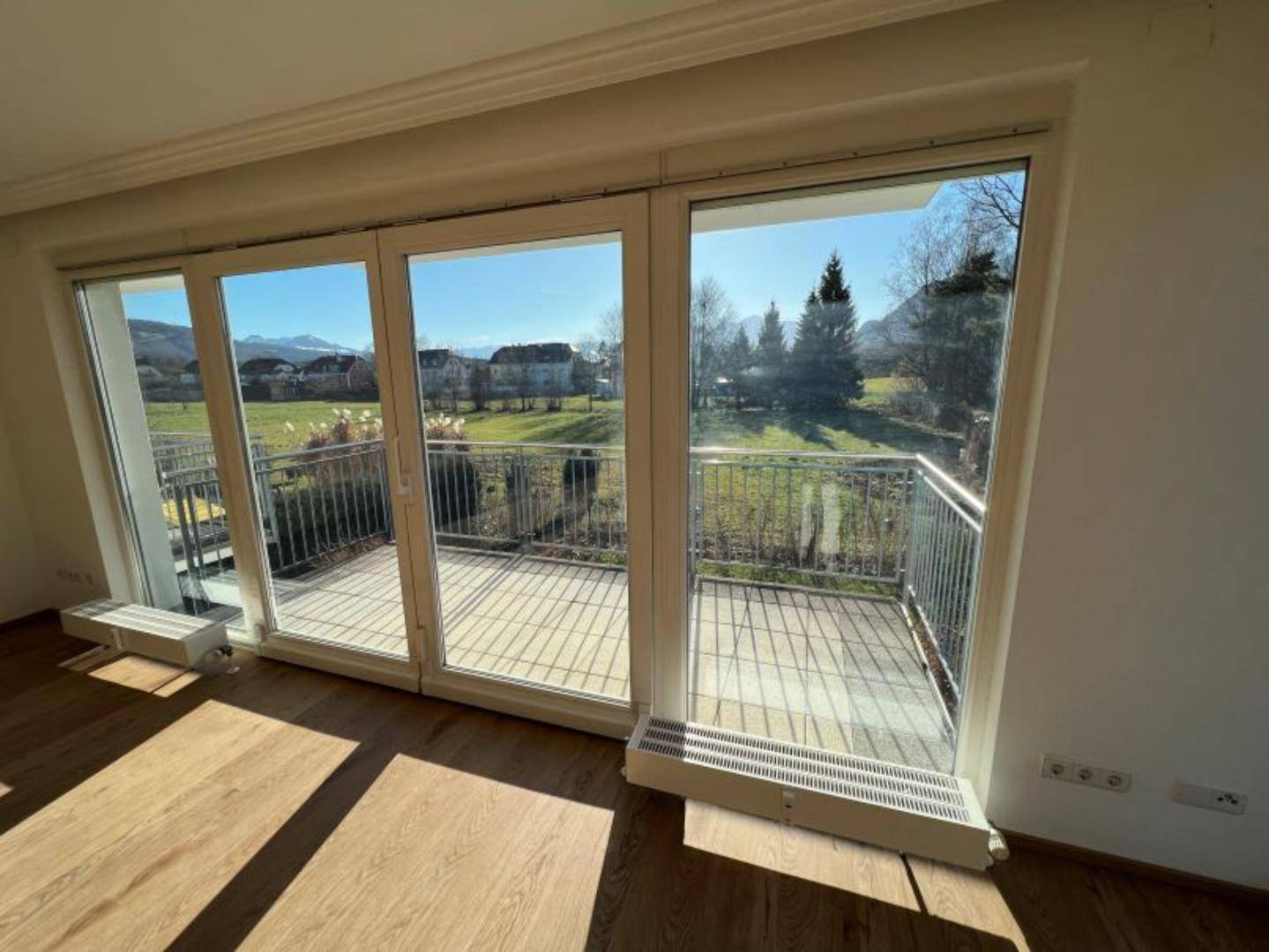 Lichtdurchfluteter Wohnbereich mit großen Fenstern und Zugang zum sonnigen Balkon.