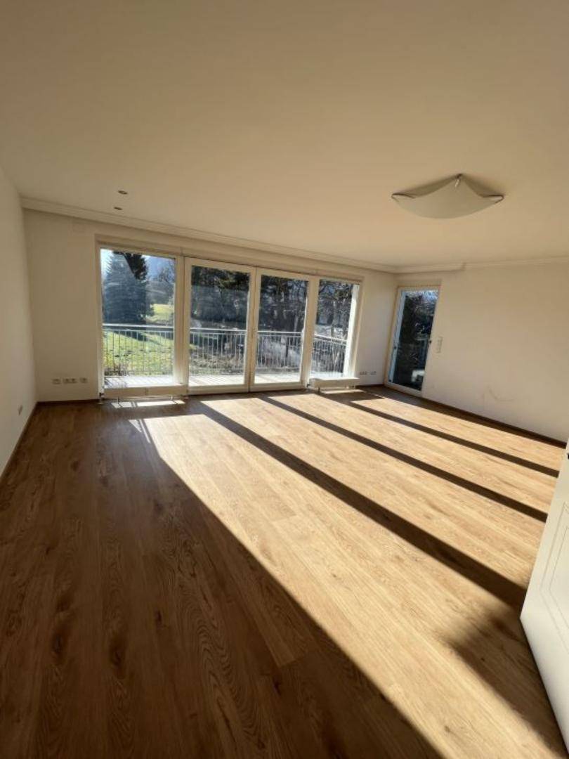 Geräumiges Wohnzimmer mit hellem Eichenparkett und großen Fenstern zum Balkon.