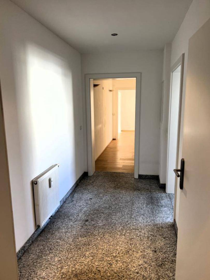 Flur mit grauem Terrazzoboden, weißen Wänden und Heizkörper.
