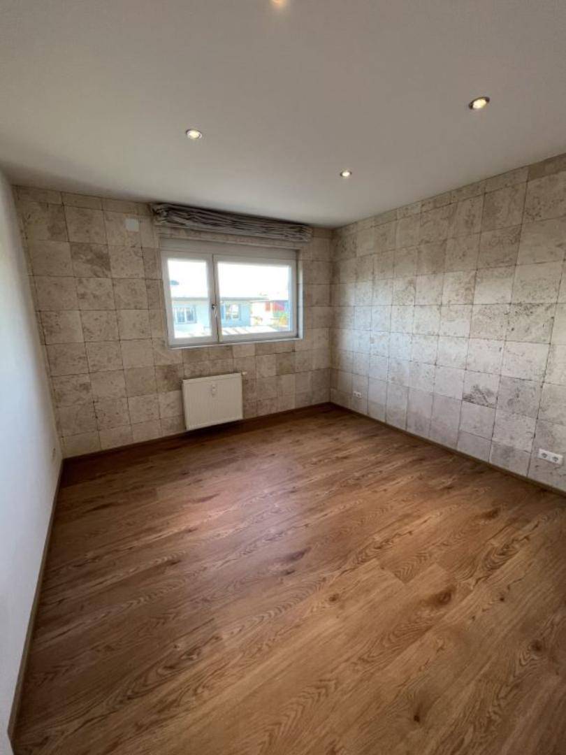 Schlafzimmer mit Holzboden, einer Akzentwand in Steinoptik und einem Fenster.