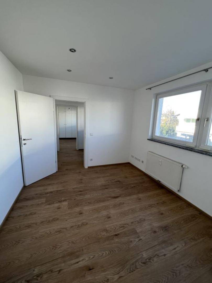 Helles Schlafzimmer mit Eichenparkettboden, weißen Wänden und einem Fenster.