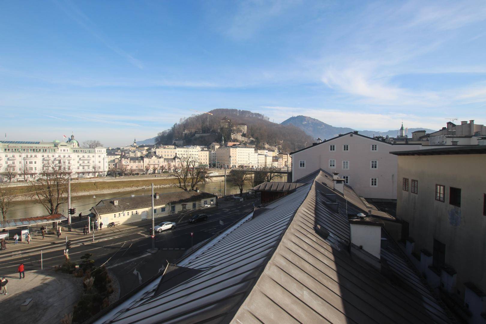 Panoramablick über die Stadt Salzburg mit Fluss, historischen Gebäuden und Bergen im Hintergrund.