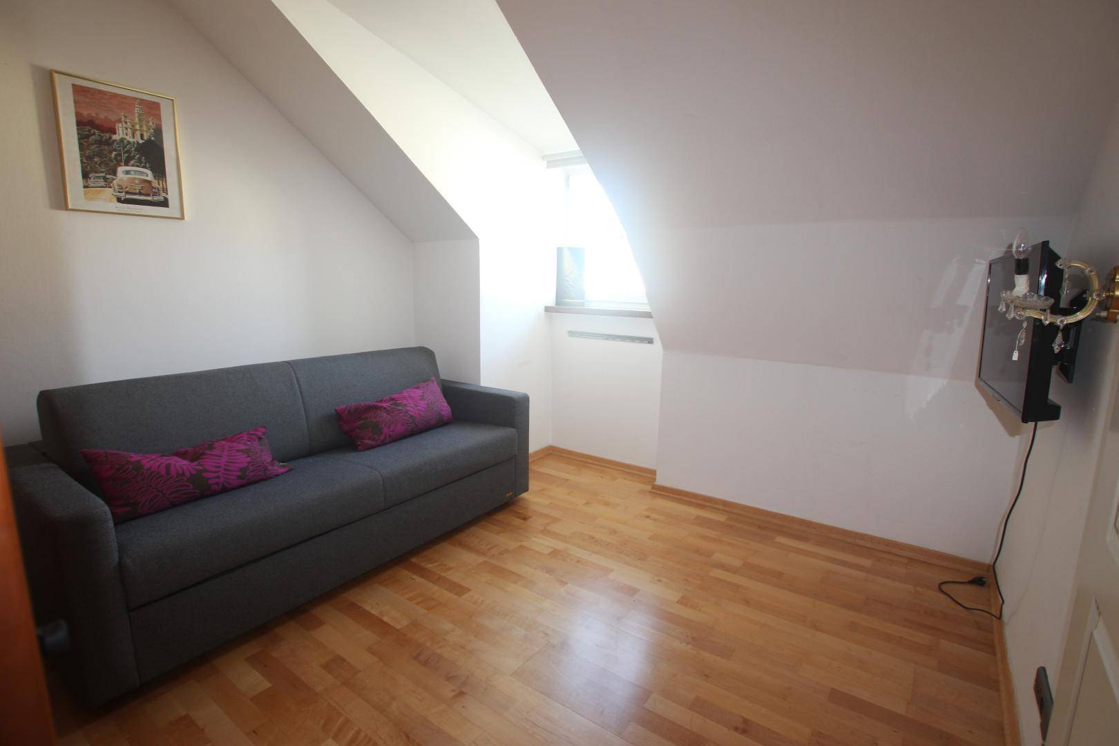 Kleines Zimmer mit Schlafsofa, Holzboden und schrägen Wänden im Dachgeschoss.