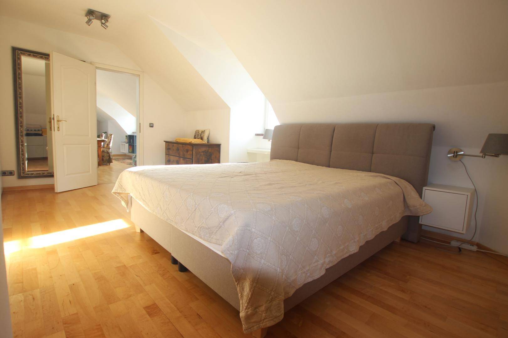 Gemütliches Schlafzimmer mit großem Bett, Holzboden und schrägen Dachschrägen.
