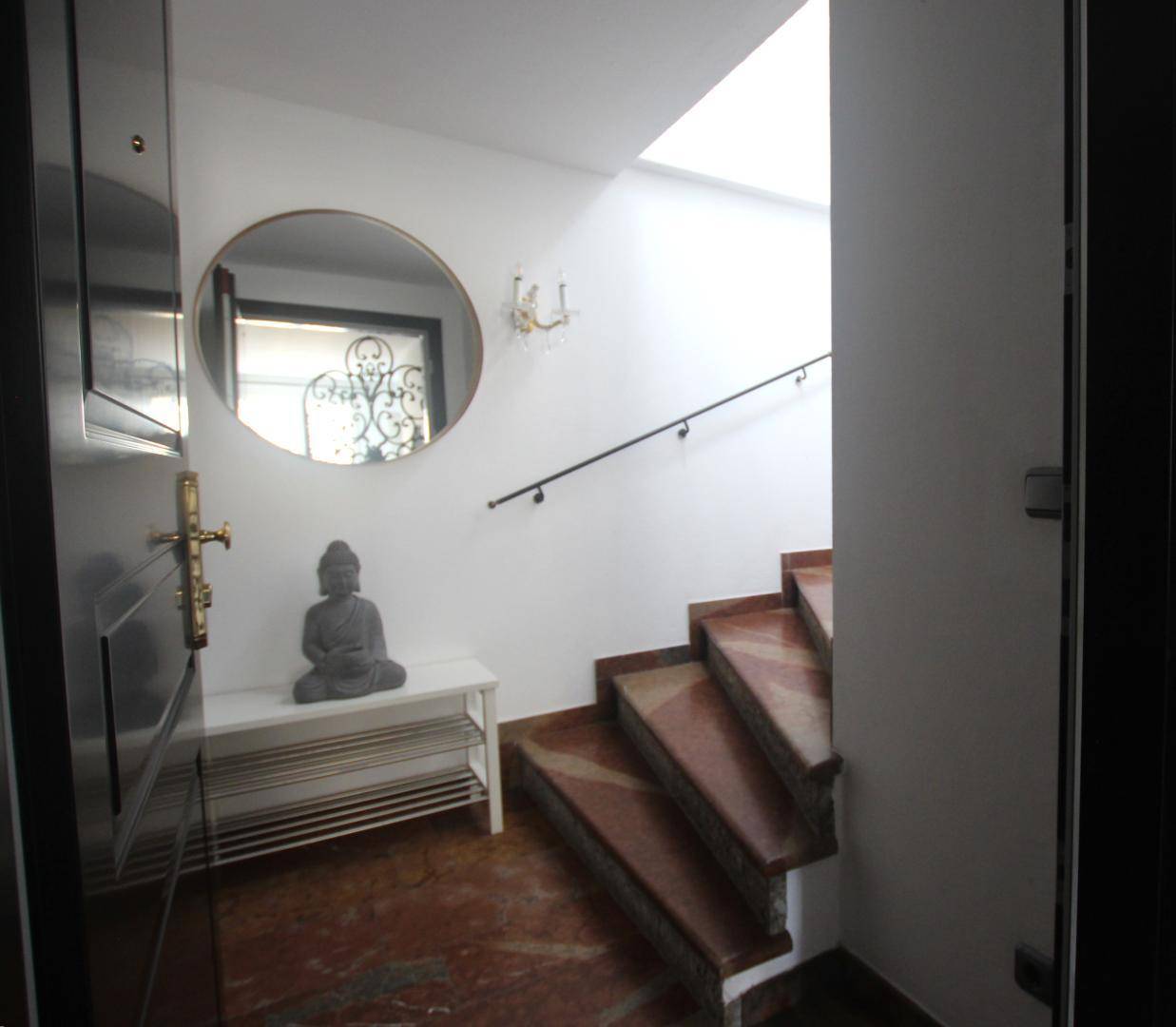 Heller Eingangsbereich mit Marmorboden, einer Treppe und einem runden Spiegel.