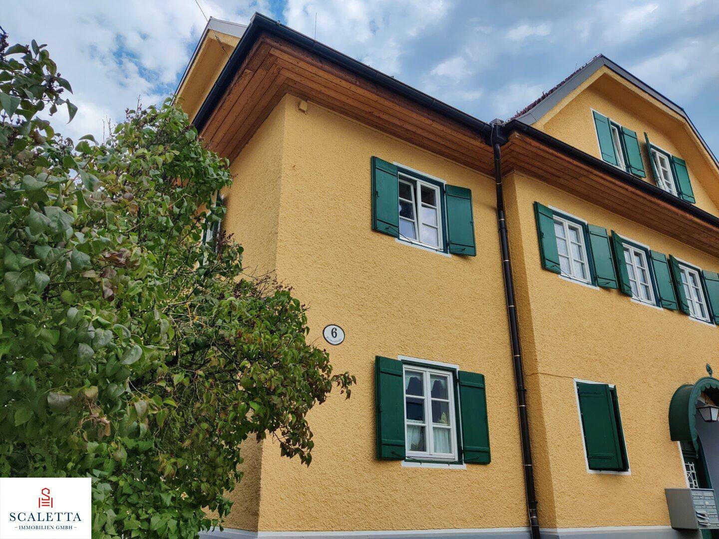 Gelbes Gebäude mit grünen Fensterläden und traditioneller Architektur, umgeben von Bäumen.