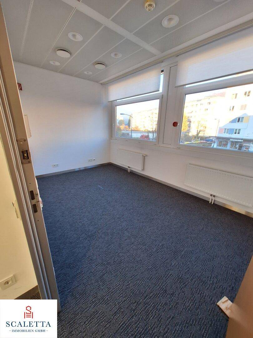 Helles Einzelbüro mit Teppichboden, Heizkörpern und Blick auf die Stadt.