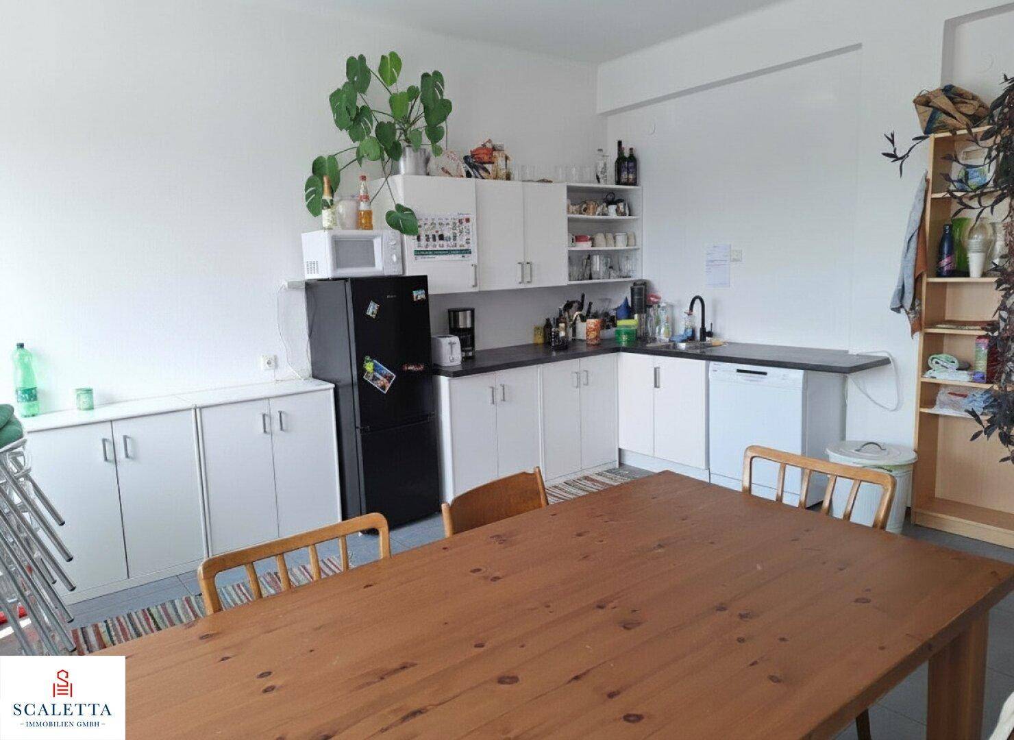 Funktionale Küche mit weißen Schränken, schwarzer Arbeitsplatte und einem Holztisch für Pausen.