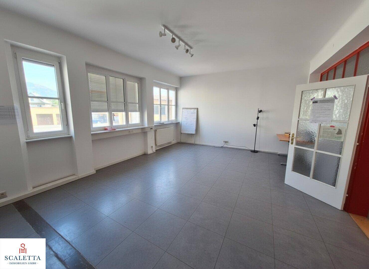 Großer, leerer Büroraum mit mehreren Fenstern und grauen Fliesen, ideal für flexible Nutzung.