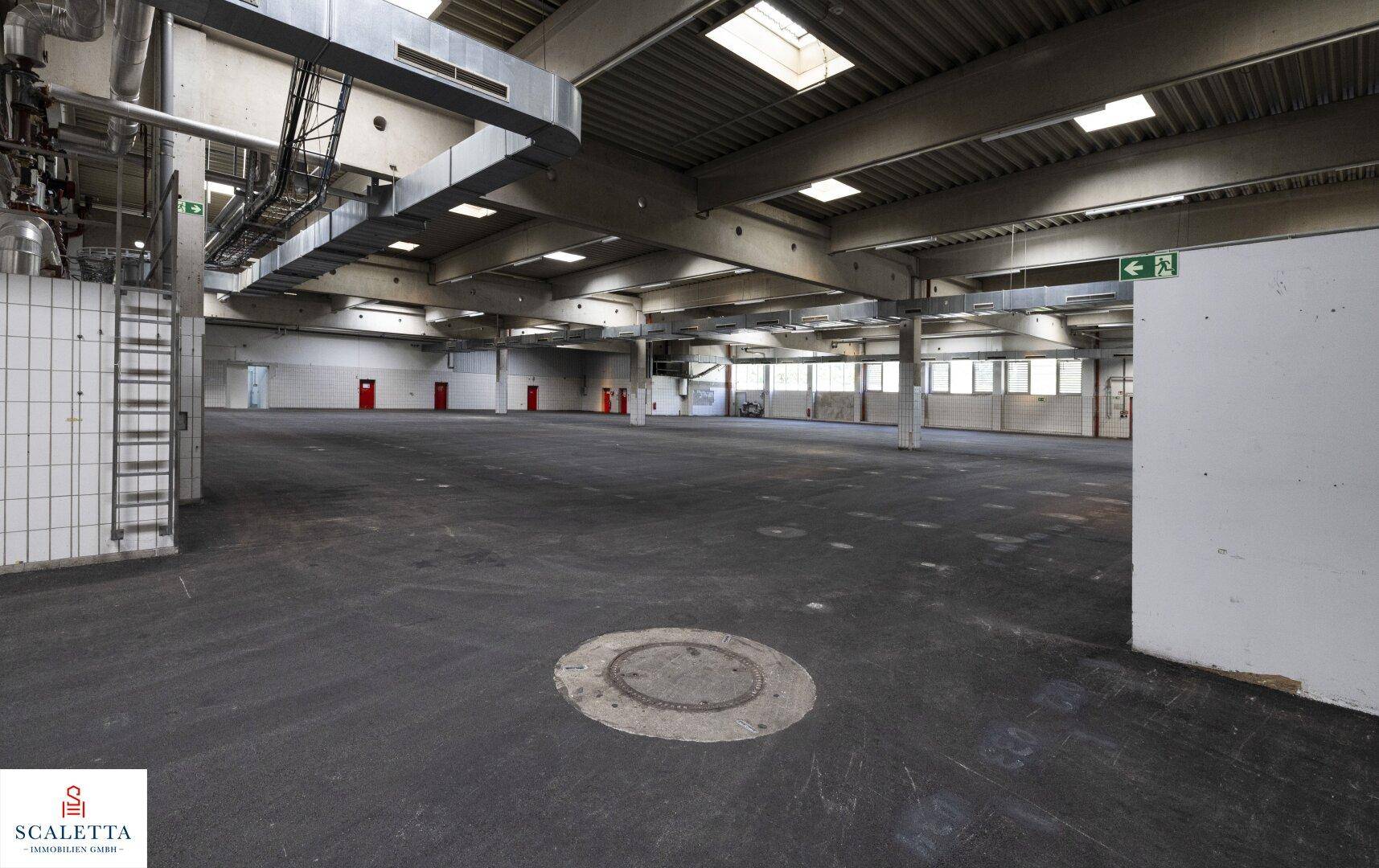 Industrielle Lagerhalle mit technischen Installationen, gefliester Wand und einem Bodenablauf.
