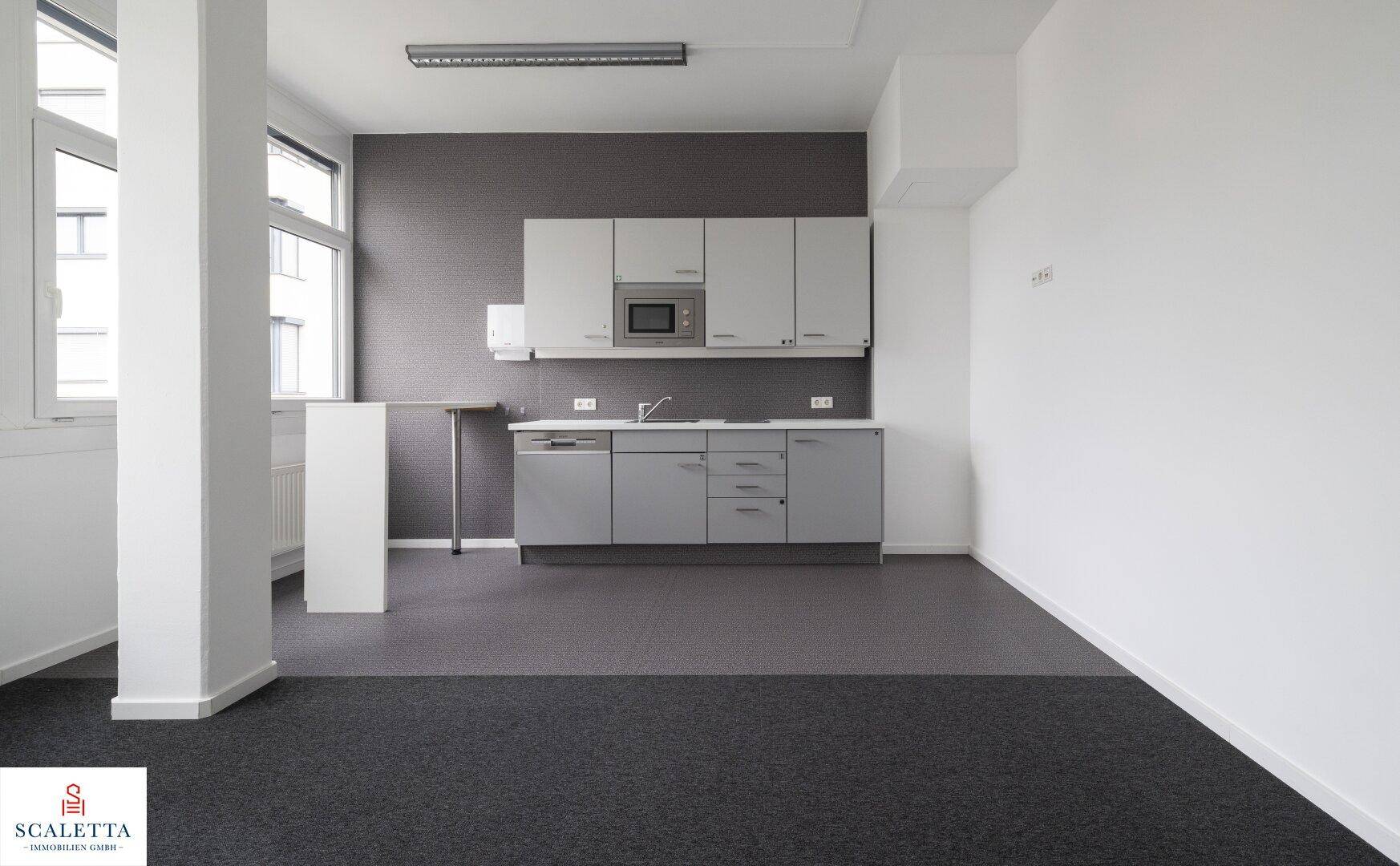 Funktionale Küchenzeile in einem Büroraum mit grauen Schränken, Mikrowelle und Spülmaschine.