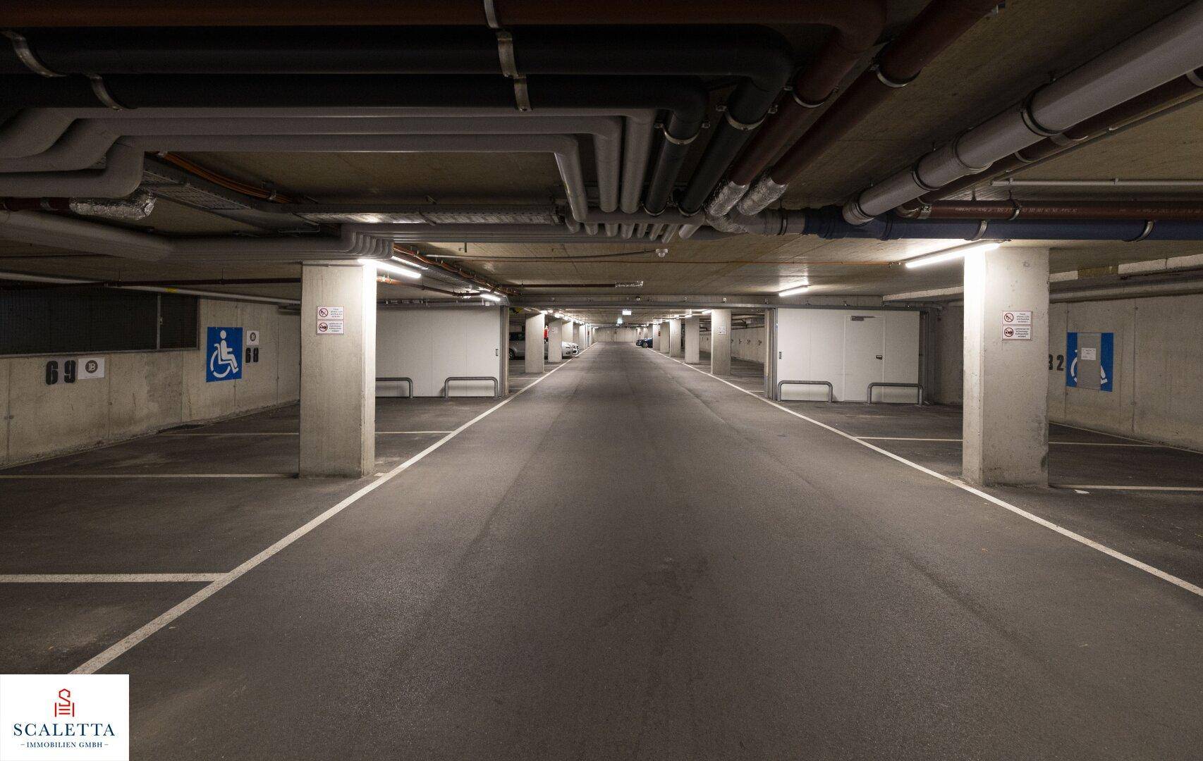 Tiefgarage mit Betonpfeilern, markierten Parkplätzen und sichtbaren Leitungen an der Decke.