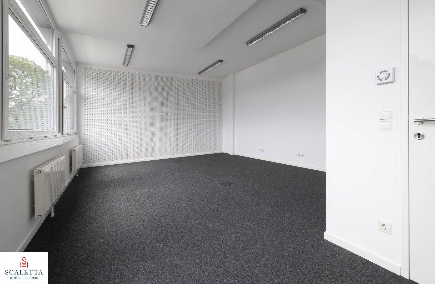 Helles Büro mit Teppichboden, weißen Wänden und einem Fenster, ausgestattet mit einem Temperaturregler.