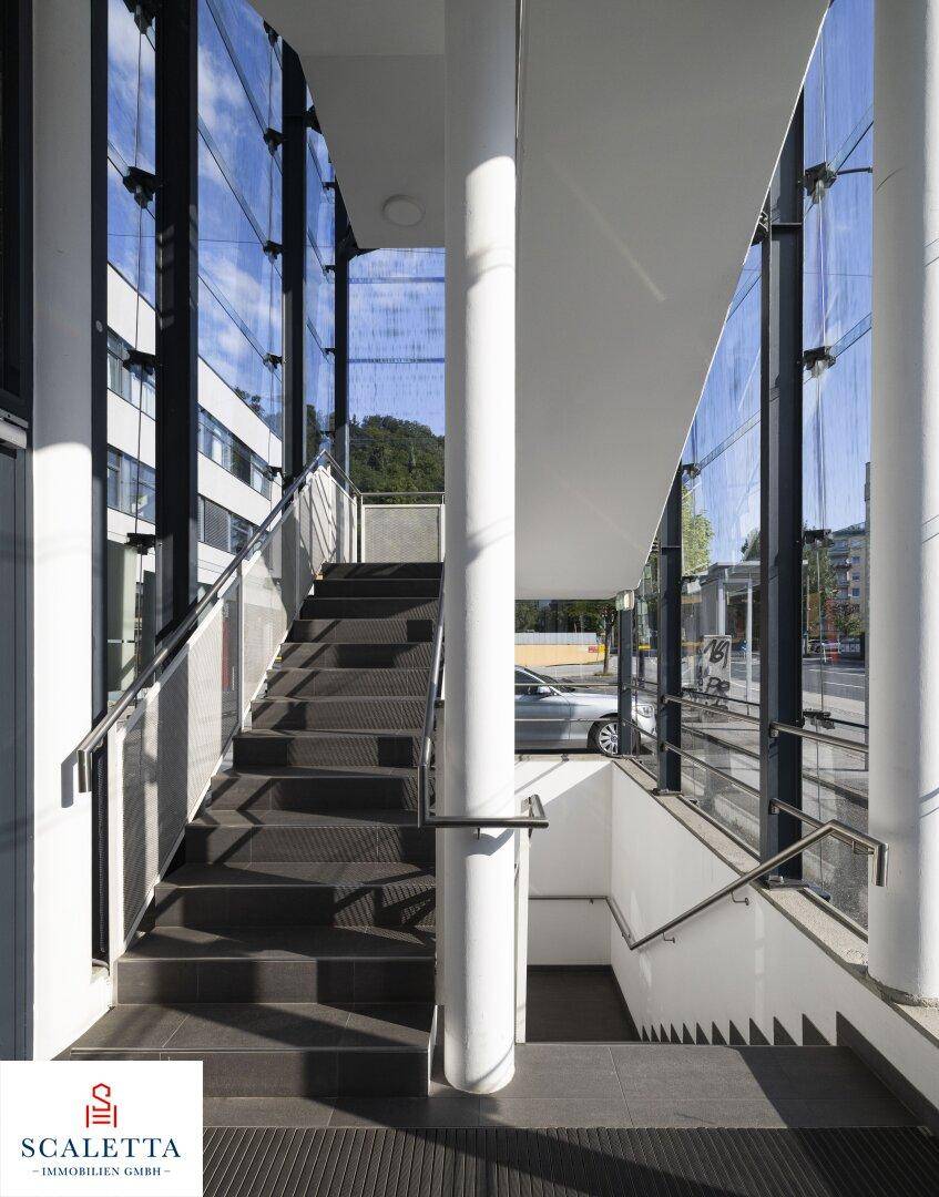 Modernes Treppenhaus mit Glaswänden, Metallgeländern und dunklen Stufen, das mehrere Etagen verbindet.