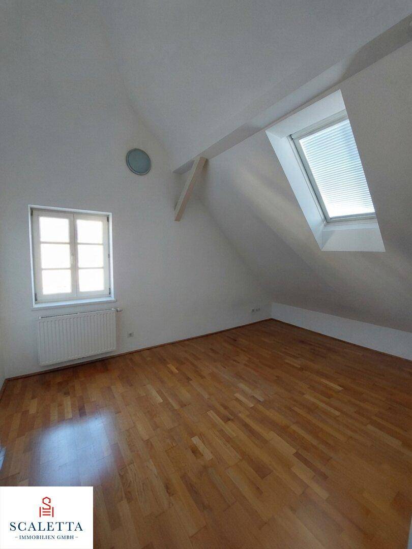 Geräumiges Dachzimmer mit Holzboden, einem traditionellen Fenster und einem zusätzlichen Dachfenster.