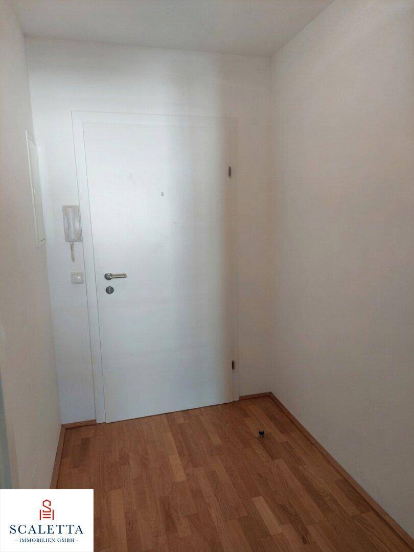 Heller Flur mit Holzboden und einer weißen Eingangstür, ausgestattet mit einer Gegensprechanlage.