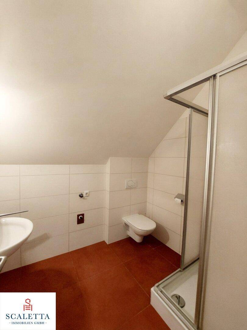 Badezimmer mit weißen Wandfliesen, terrakottafarbenem Boden, Dusche, WC und einem Waschbecken.