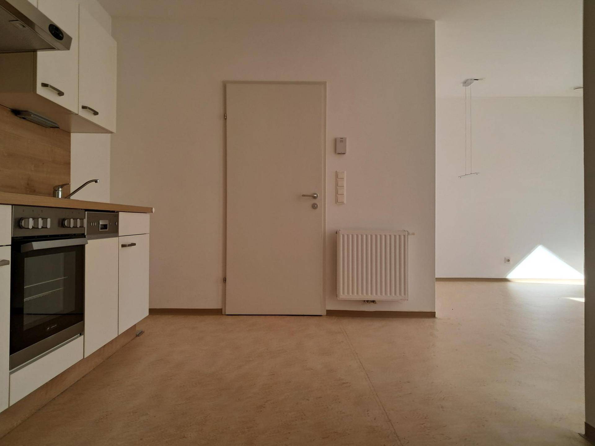 Heller Raum mit Küchenzeile auf der linken Seite und Zugang zu einem weiteren Bereich.
