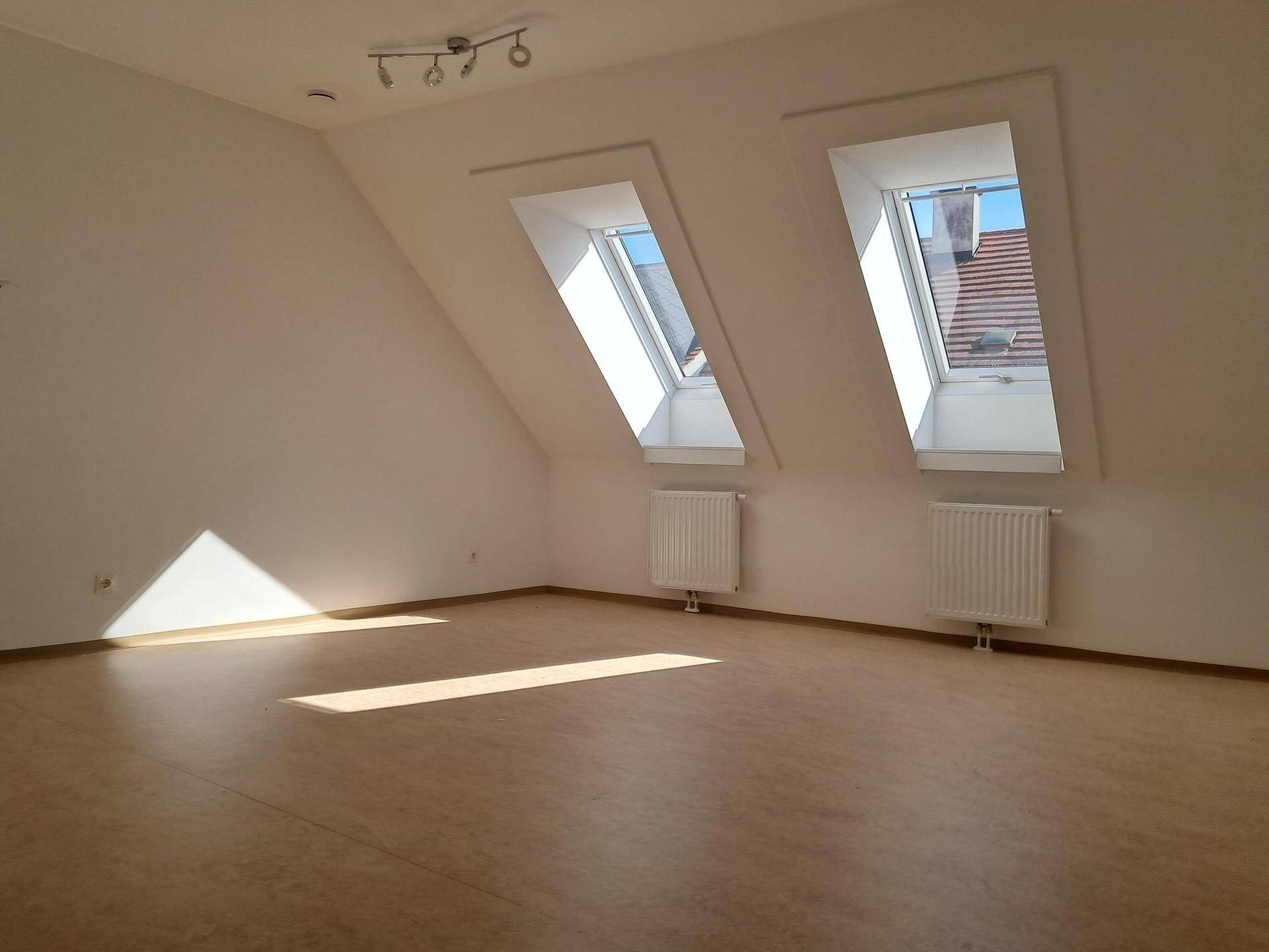 Geräumiger Wohnbereich im Dachgeschoss mit zwei großen Dachfenstern und viel Tageslicht.