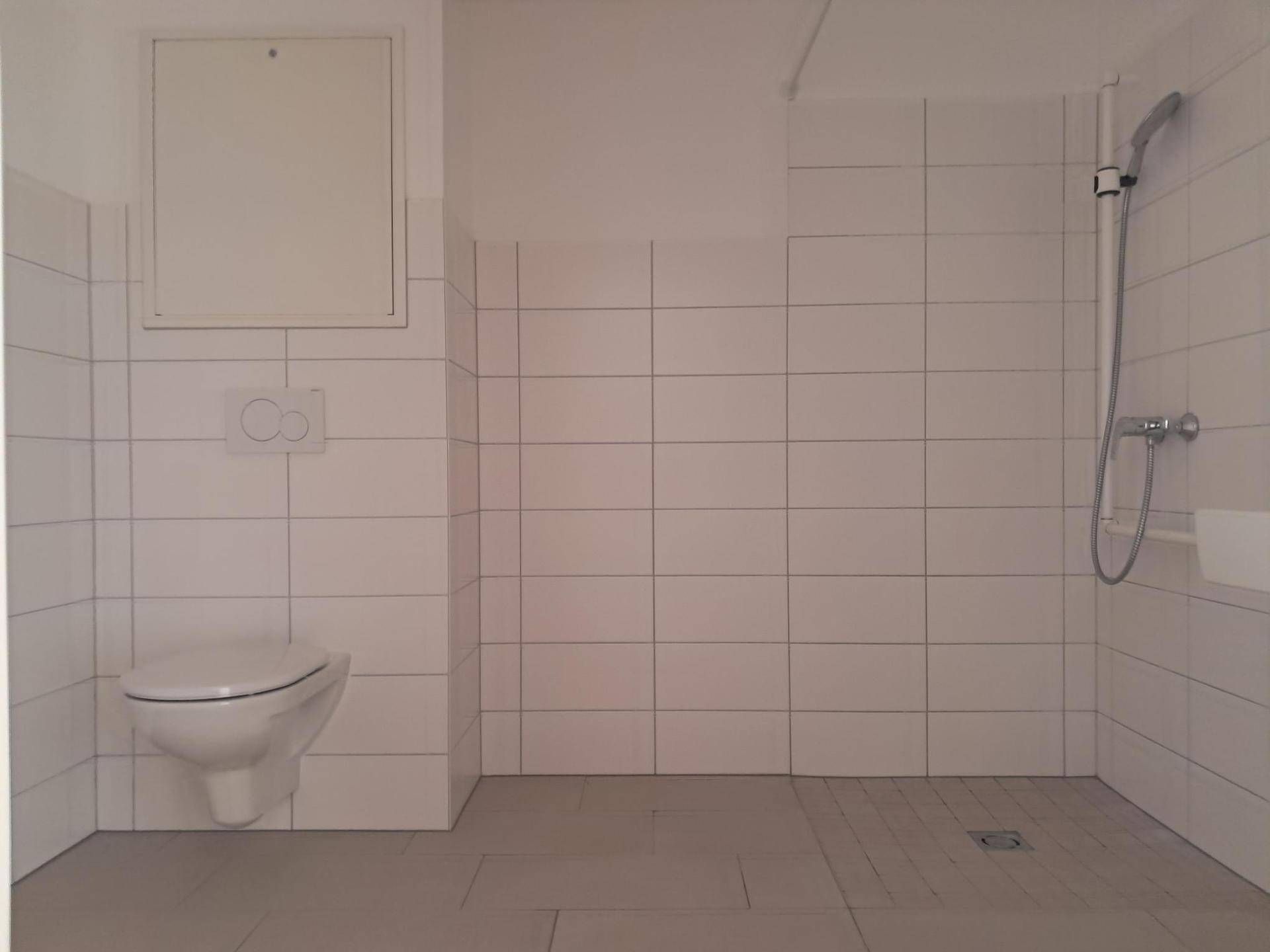 Helles Badezimmer mit wandhängendem WC und ebenerdiger Dusche, komplett gefliest.