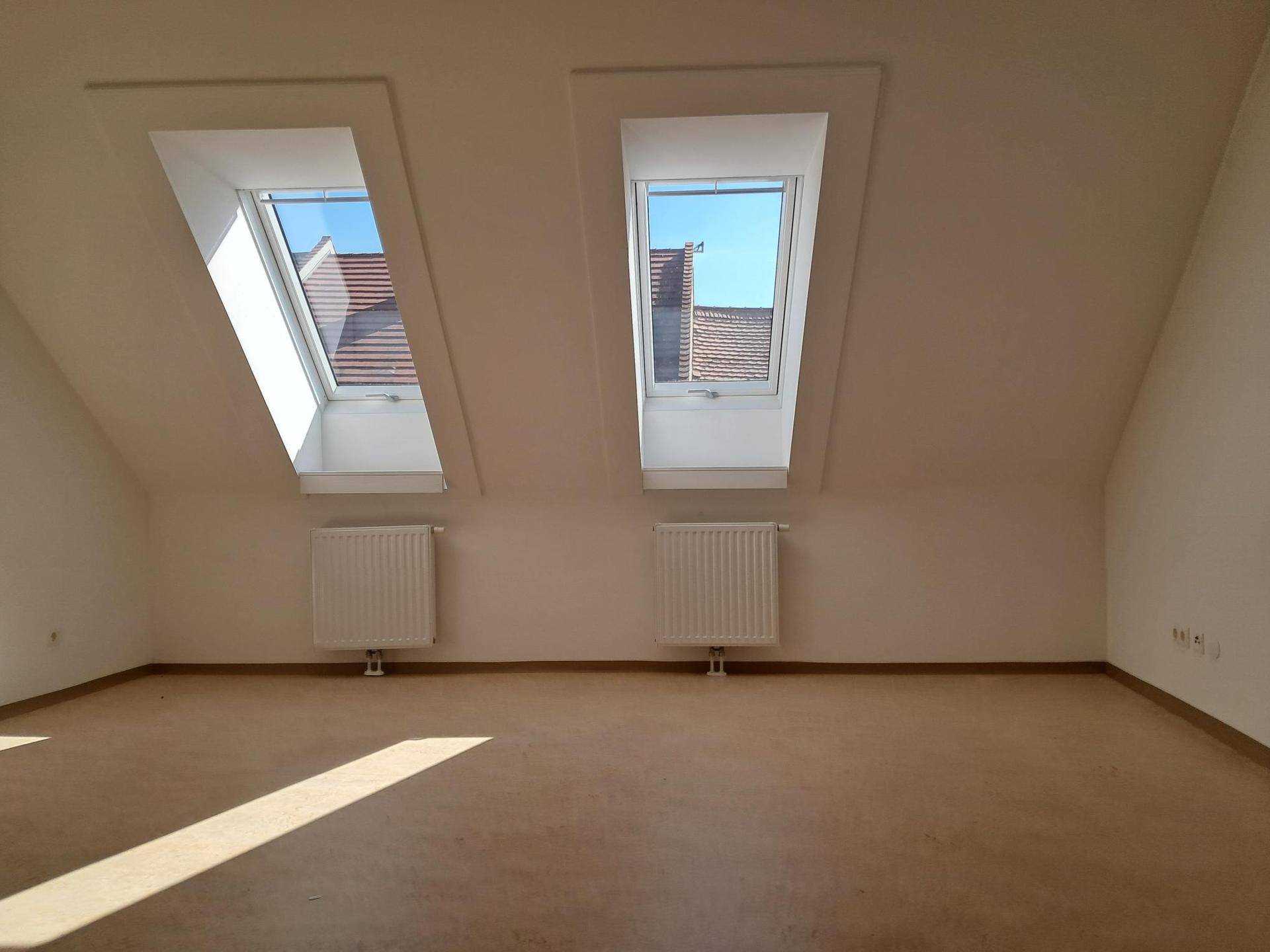 Heller Dachgeschossraum mit zwei großen Dachfenstern, die viel Sonnenlicht hereinlassen.