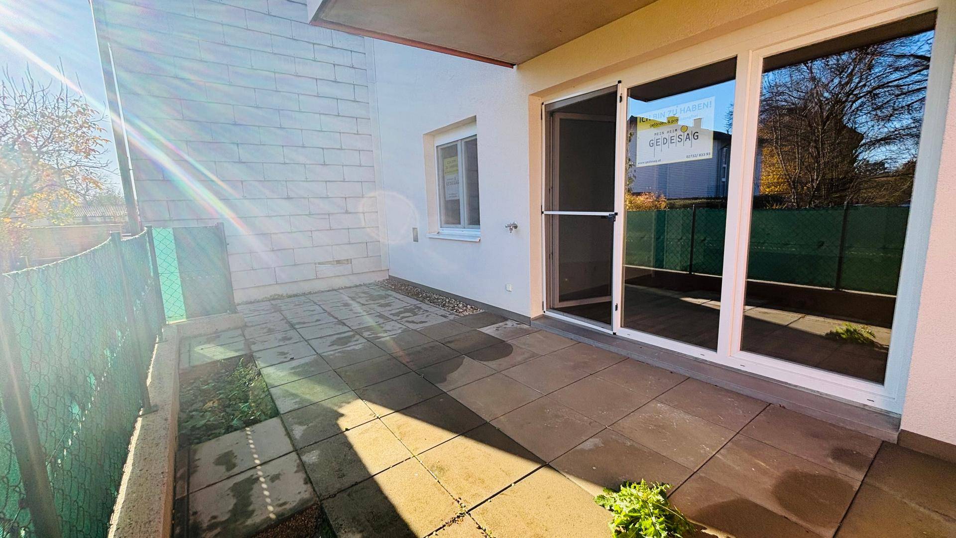 Sonniger Terrassenbereich mit Steinplatten und direktem Zugang zum Garten.