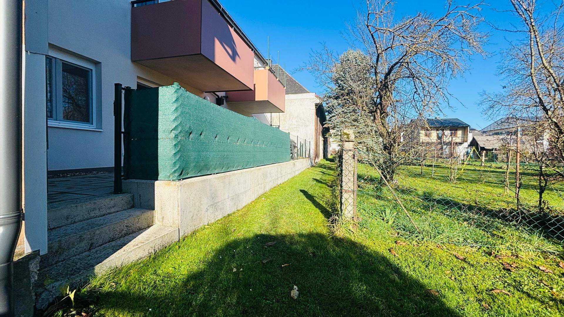 Grüner Gartenbereich neben der Terrasse mit Rasenfläche und Bäumen im Hintergrund.