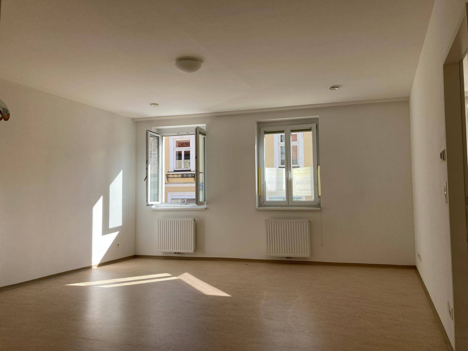 Lichtdurchfluteter Wohnraum mit zwei Fenstern, die viel Tageslicht hereinlassen und Blick auf die Umgebung bieten.