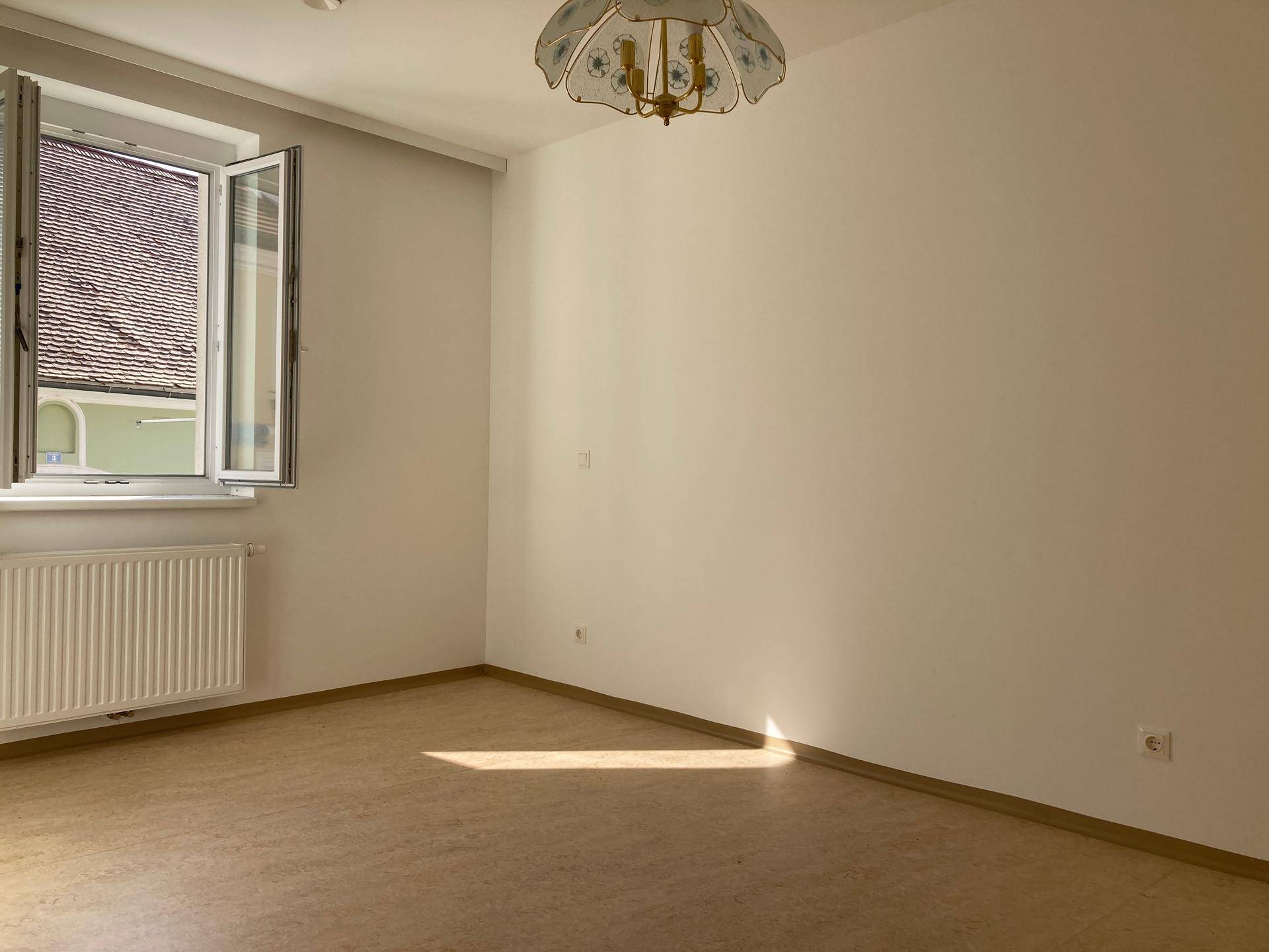 Helles Schlafzimmer mit einem Fenster, das einen Blick auf ein Dach und viel Sonnenlicht bietet.