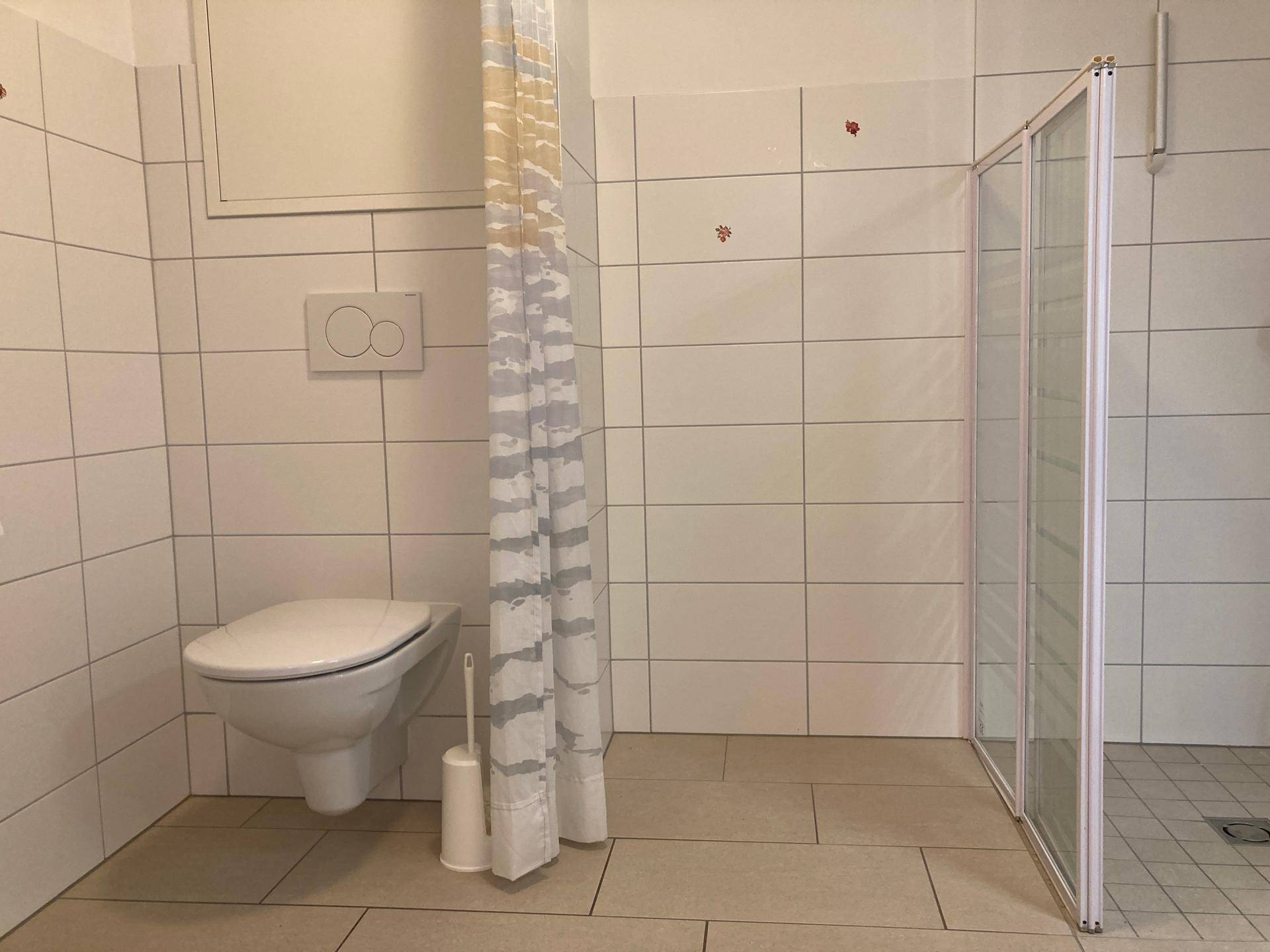 Funktionales Badezimmer mit wandhängender Toilette und einer Duschkabine.