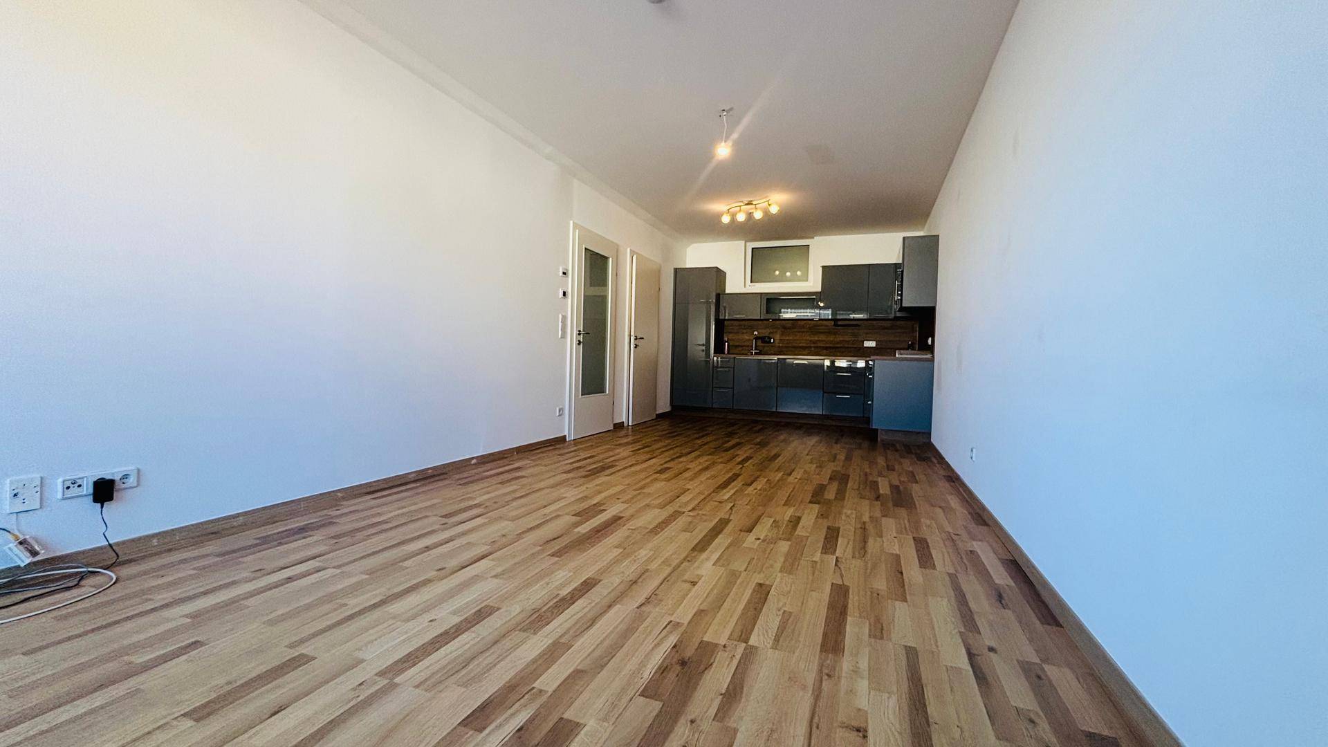 Geräumiger offener Wohnbereich mit integrierter Küche und hellem Parkettboden, bereit zur individuellen Gestaltung.