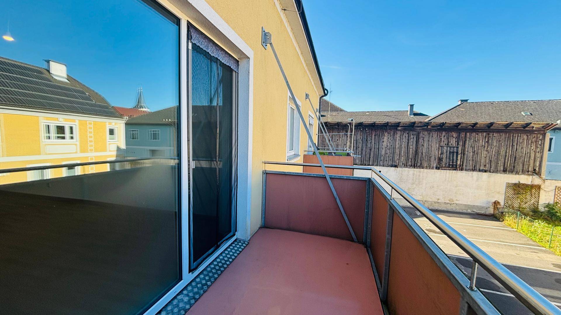 Kleiner Balkon mit Metallgeländer und Blick auf die umliegenden Gebäude und den blauen Himmel.