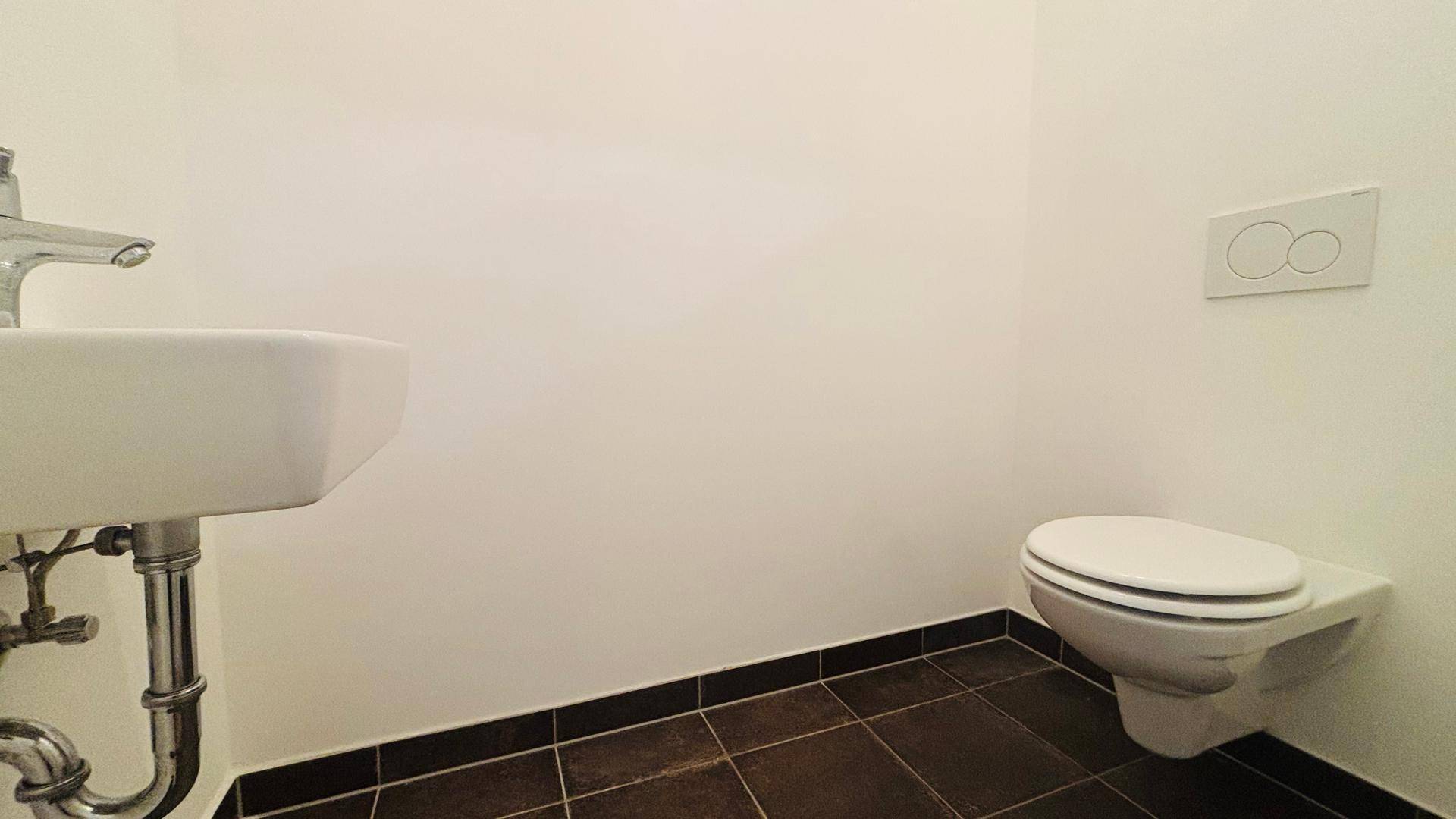Separates Gäste-WC mit wandhängender Toilette und Waschbecken, ausgestattet mit dunklen Bodenfliesen.