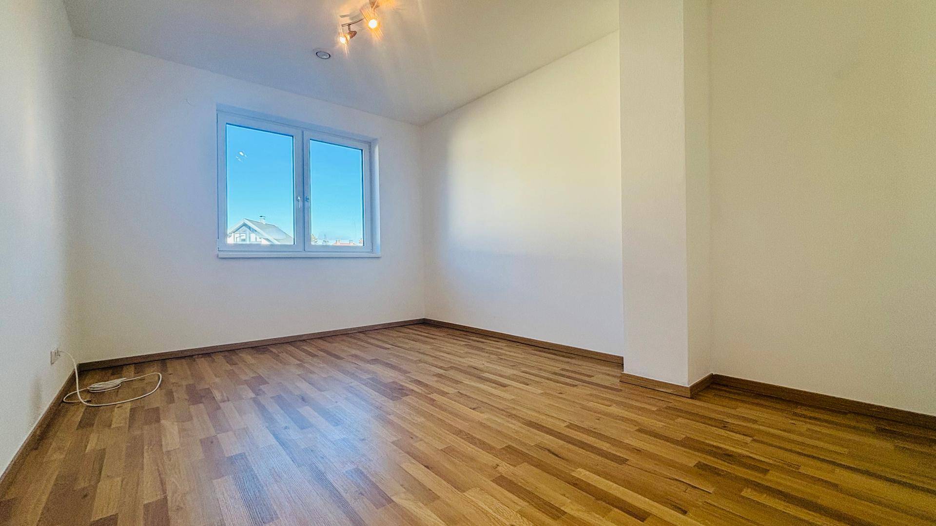 Freundliches Schlafzimmer mit Parkettboden und großem Fenster, das viel Tageslicht hereinlässt.