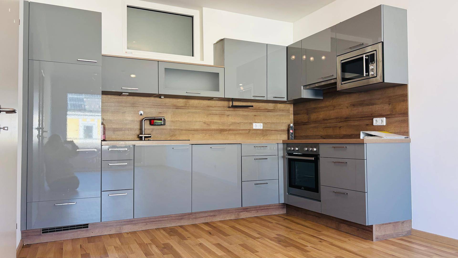 Moderne Einbauküche in Grau mit Holzoptik-Arbeitsplatte und integrierten Geräten, inklusive Mikrowelle und Backofen.