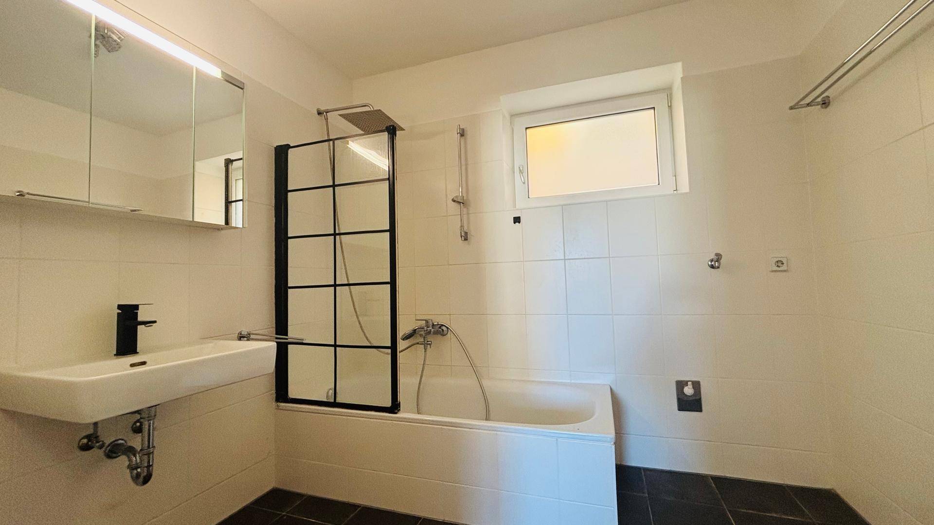 Modernes Badezimmer mit Badewanne, Duschabtrennung und Fenster, ausgestattet mit einem Spiegelschrank.