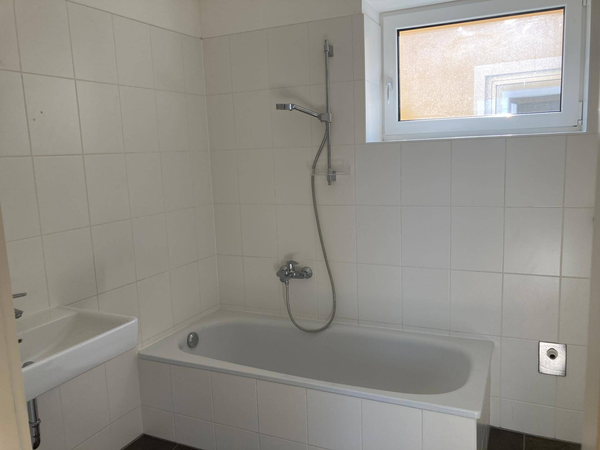 Badezimmer mit Badewanne, Waschbecken und weiß gefliesten Wänden, ausgestattet mit einem Fenster.
