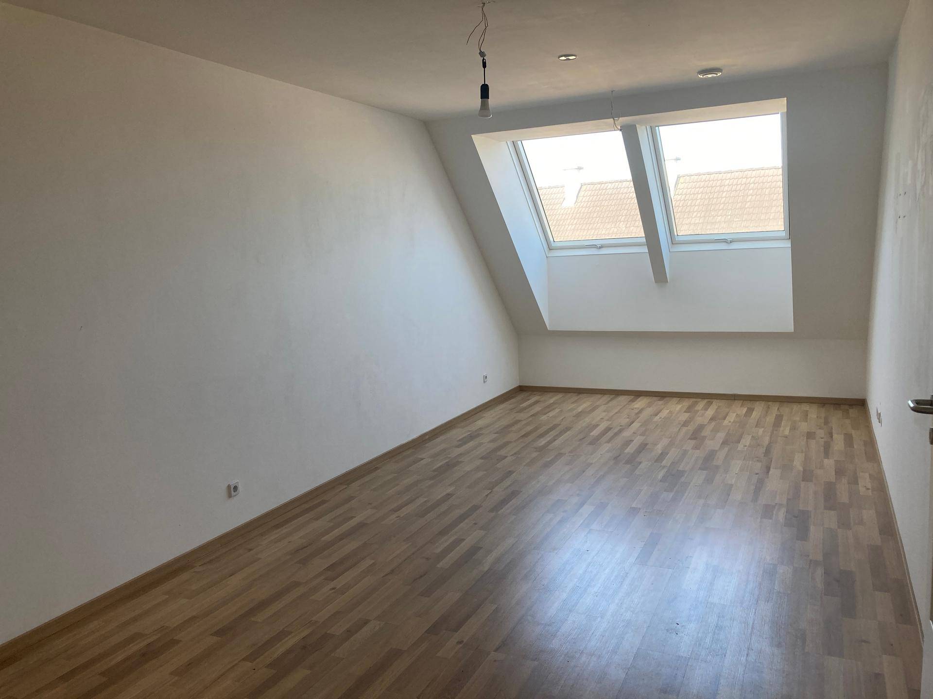 Heller Dachraum mit zwei Dachfenstern, Holzboden und schrägen Wänden, ideal als Schlaf- oder Wohnbereich.