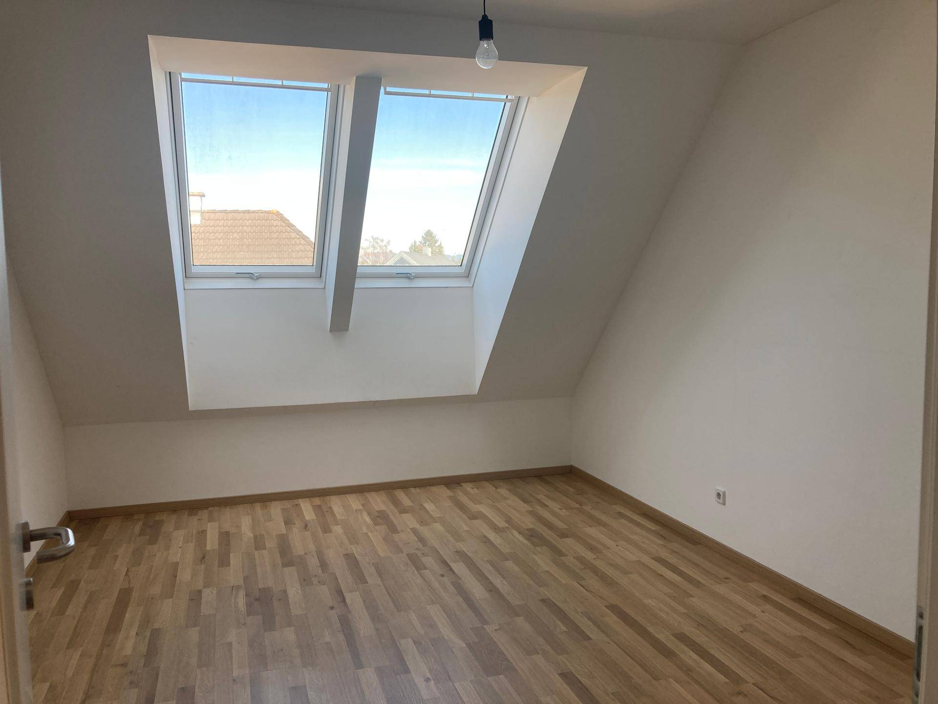 Geräumiger Dachraum mit zwei Dachfenstern, Holzboden und schrägen Wänden, ideal für ein Schlafzimmer.