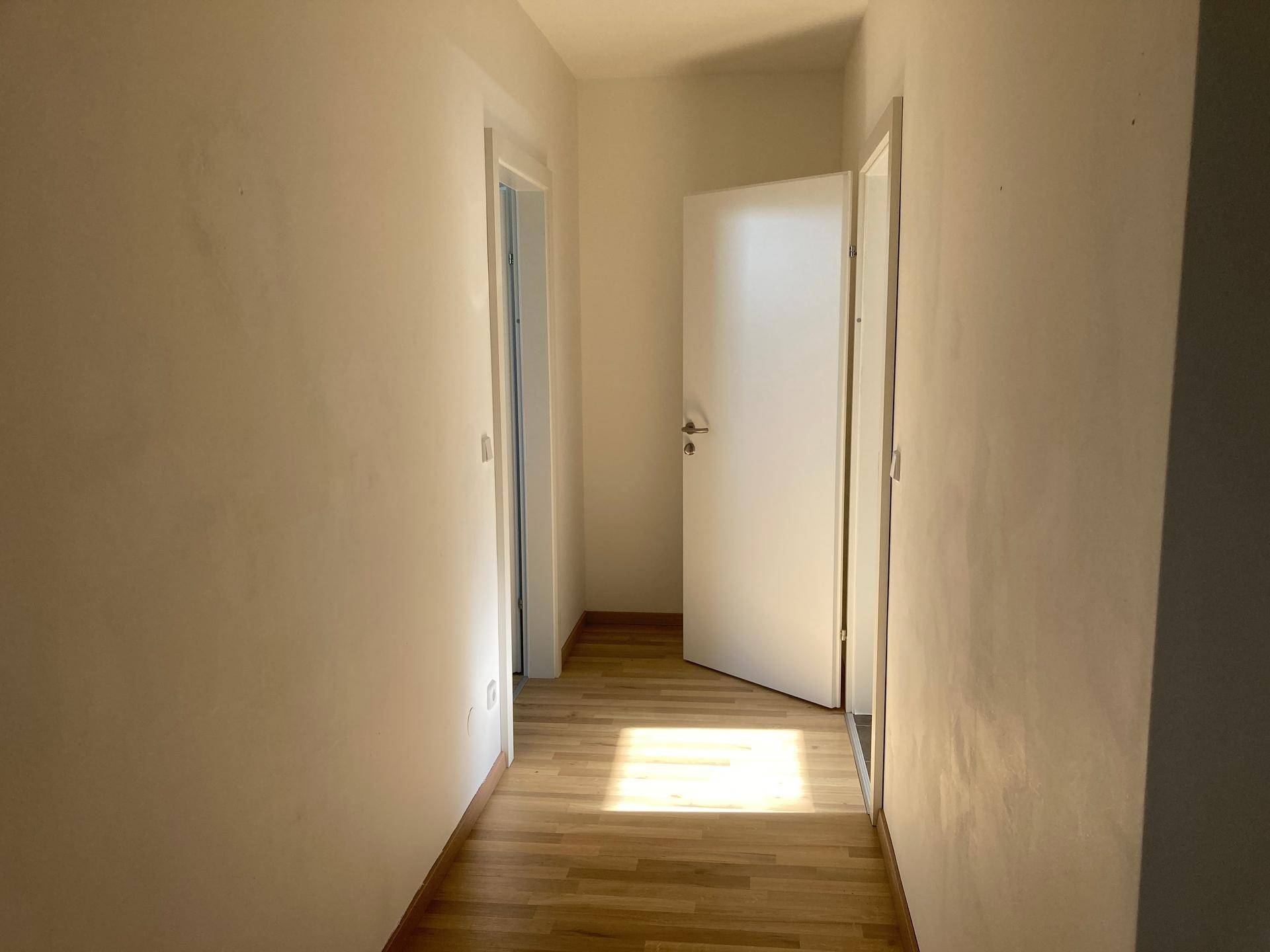 Lichtdurchfluteter Flur mit Parkettboden und offener Tür, die Sonnenlicht hereinlässt und den Raum erhellt.