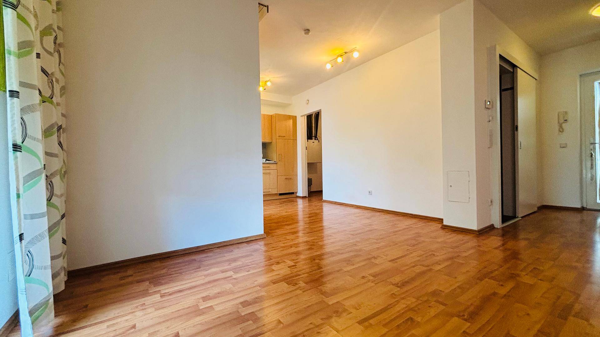 Geräumiger Wohnbereich mit warmem Holzboden und Blick auf den Küchenbereich.