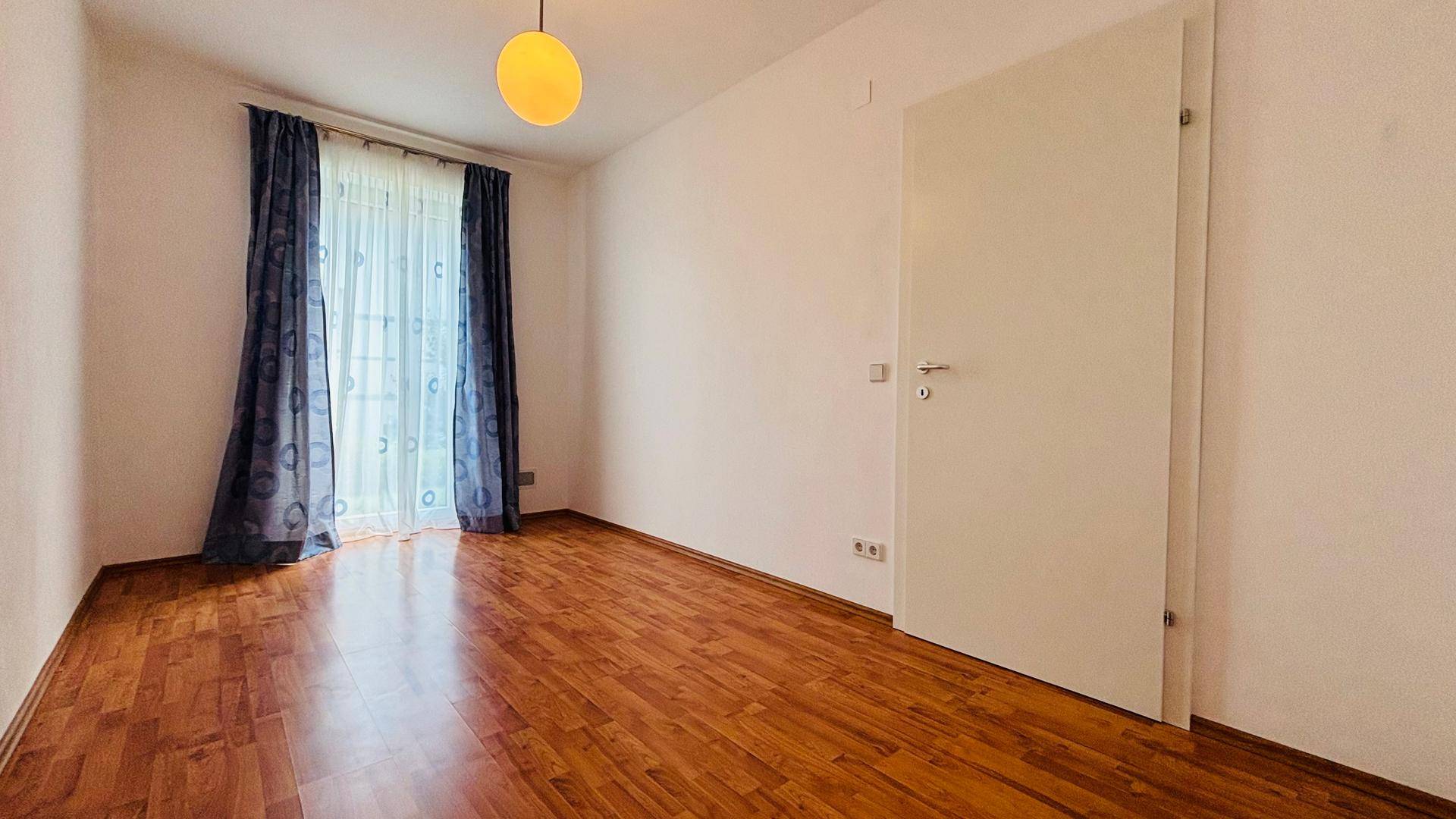 Helles, leeres Zimmer mit Holzboden und Fenster, bereit zur individuellen Gestaltung.