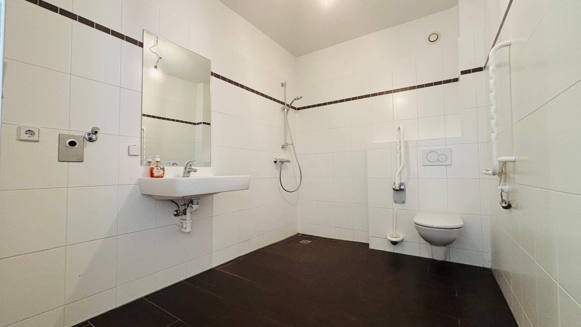Barrierefreies Badezimmer mit ebenerdiger Dusche, Wand-WC und Haltegriffen.