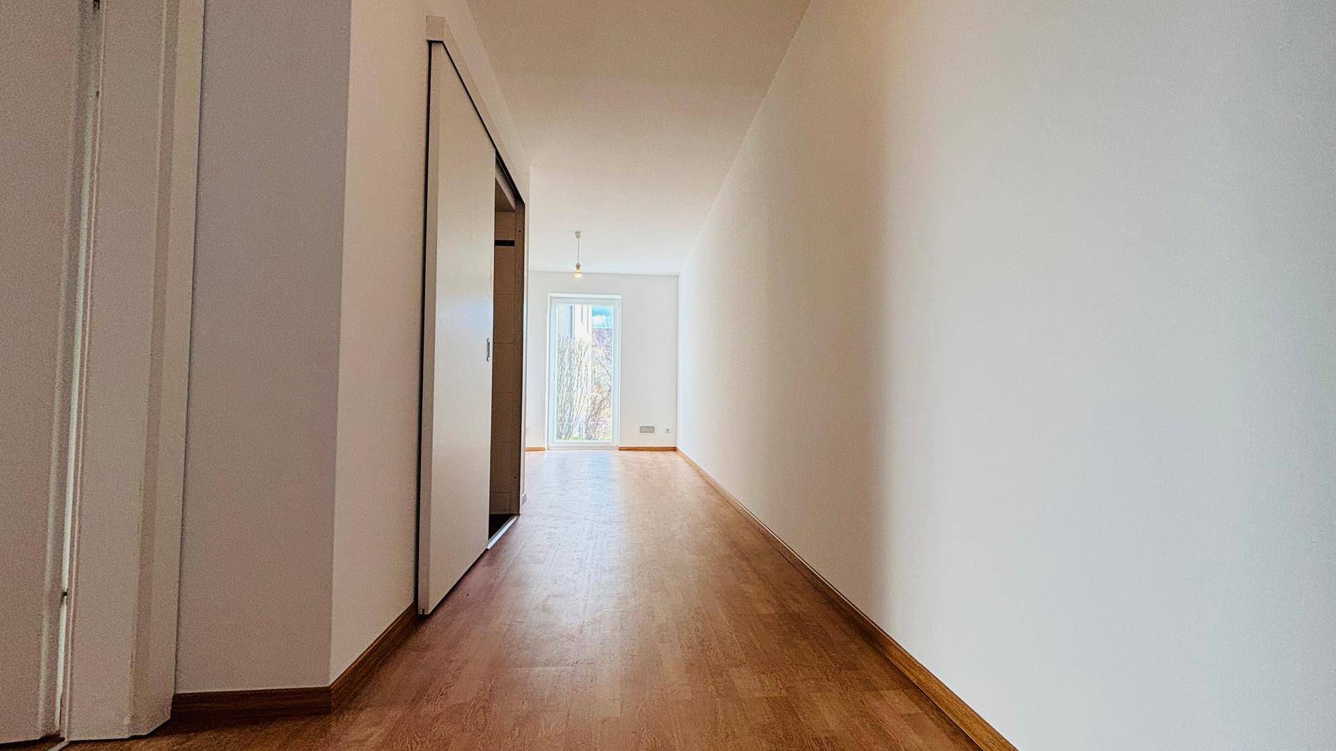 Heller Flur mit Schiebetüren und Holzboden, der zu einem weiteren Raum führt.
