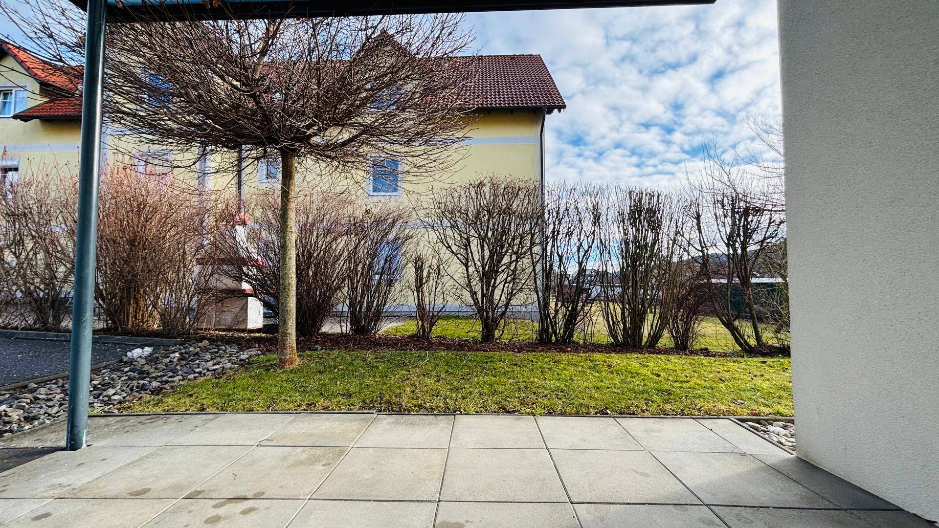 Blick von der Terrasse auf den gepflegten Rasen und ein gegenüberliegendes Gebäude.