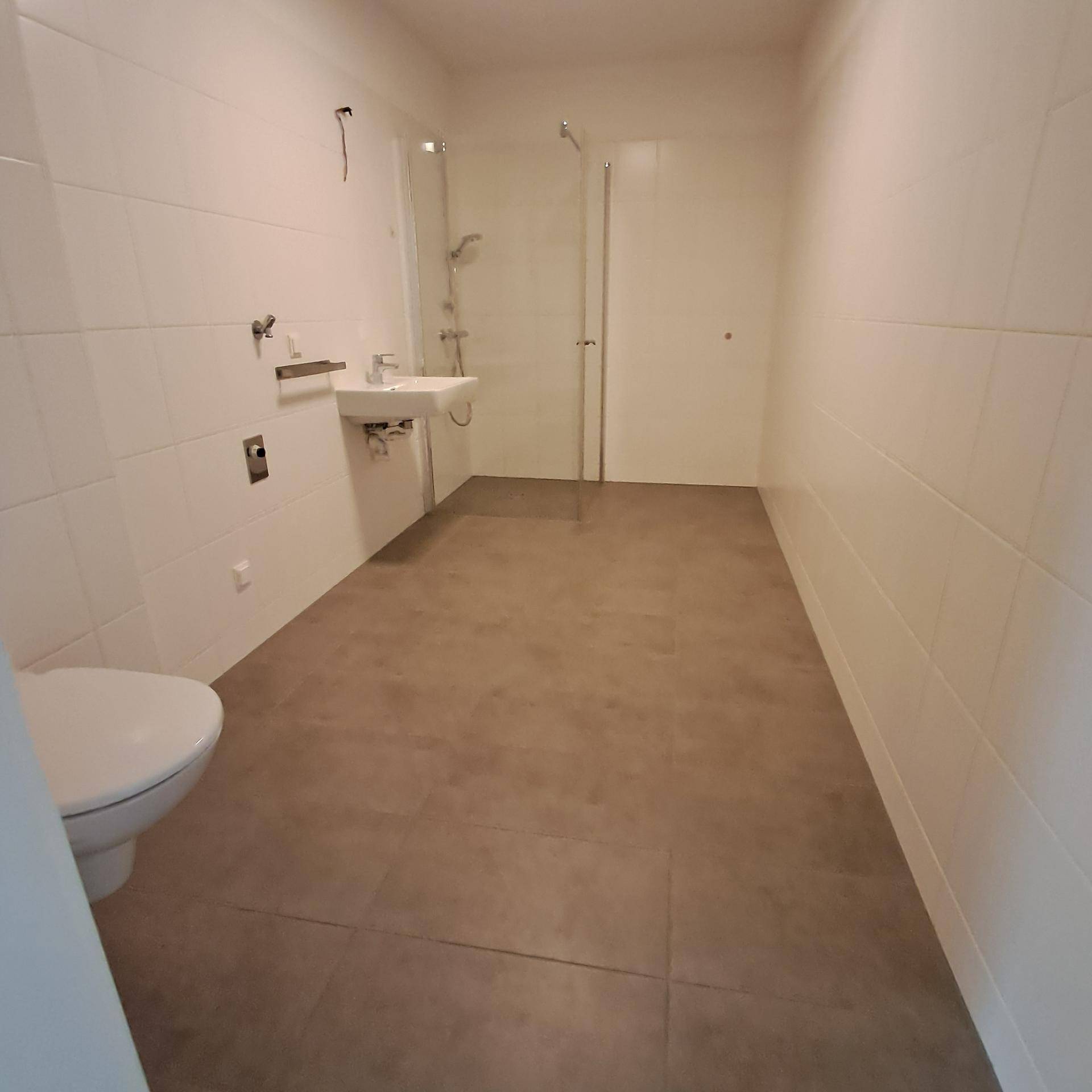 Helles Badezimmer mit weißen Fliesen, modernem WC und ebenerdiger Dusche.