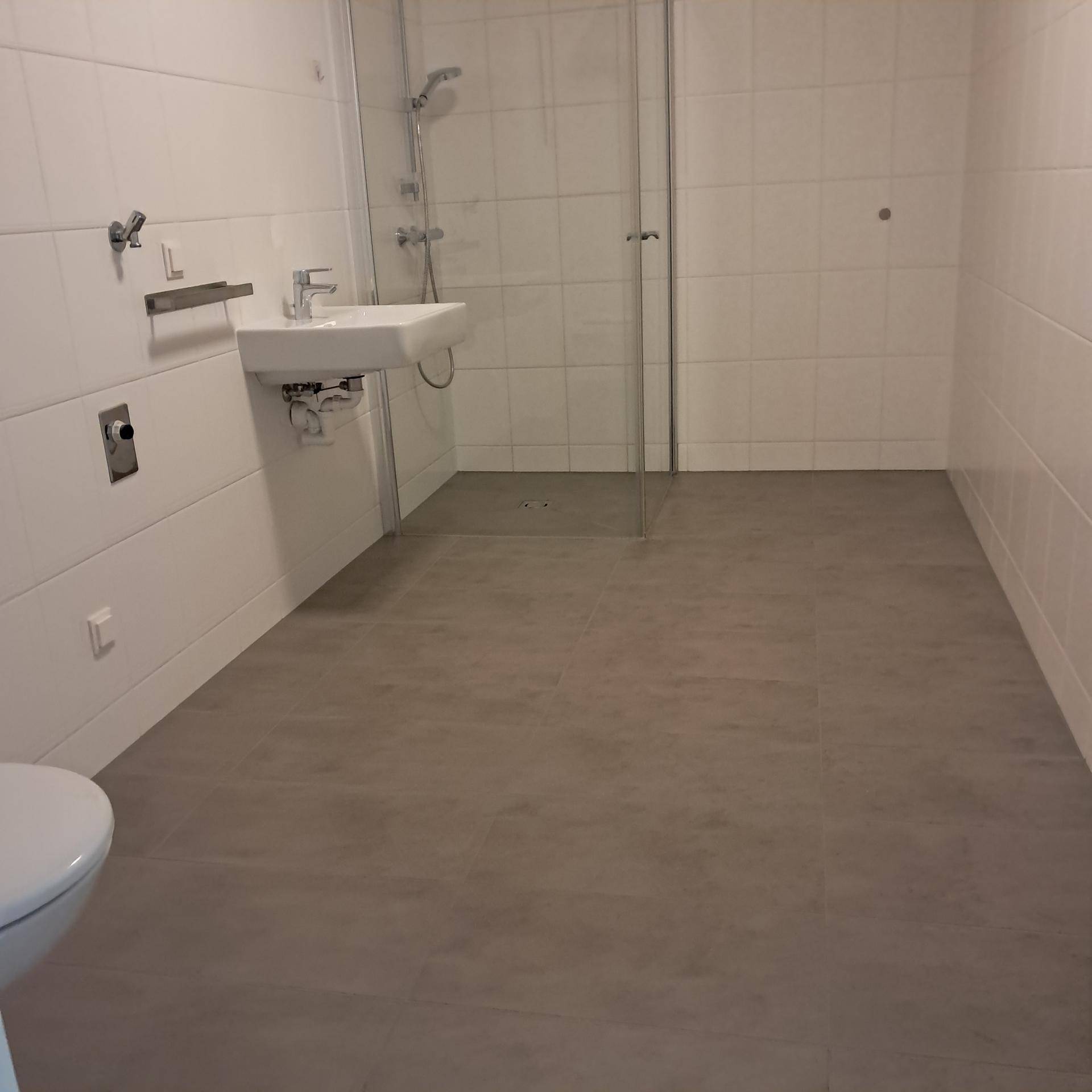 Modernes Badezimmer mit weißen Wandfliesen, Dusche und wandhängendem WC.