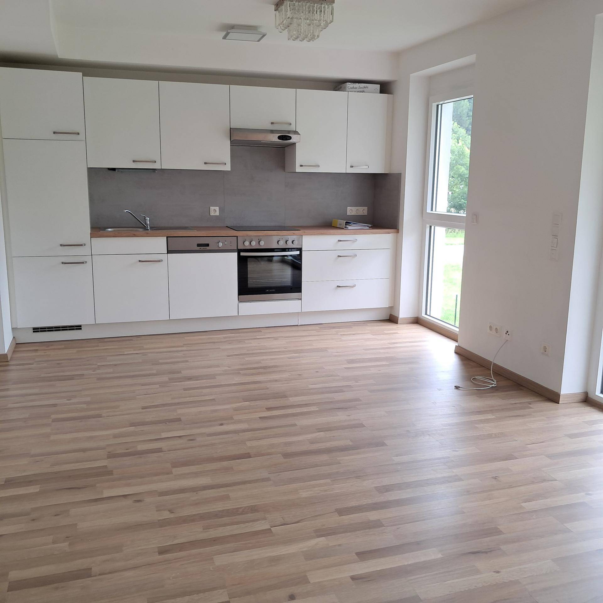 Offene Küche mit weißen Schränken, Holzarbeitsplatte und viel Tageslicht.