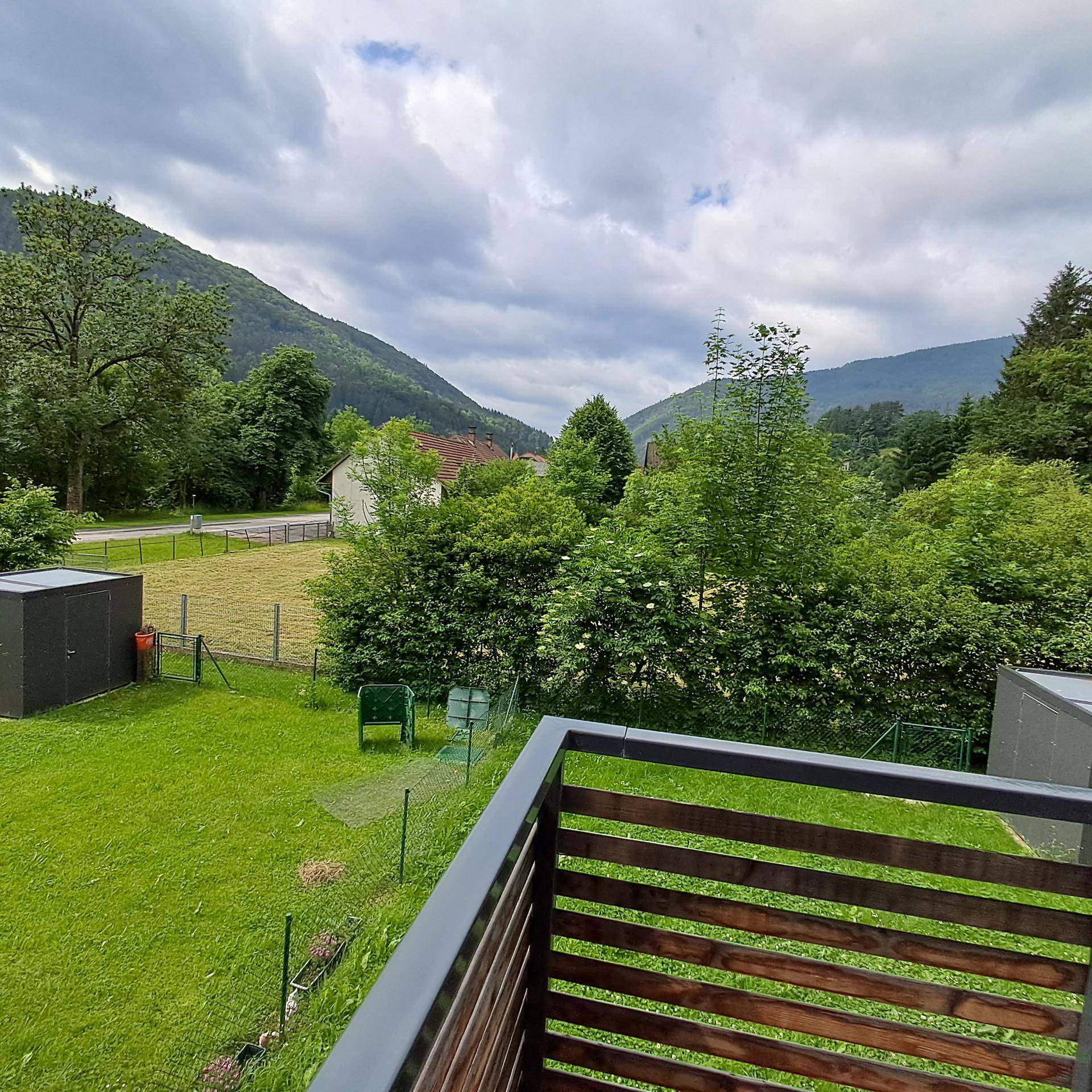 Balkon mit Holzelementen und weitem Blick auf die umliegende grüne Landschaft und Berge.